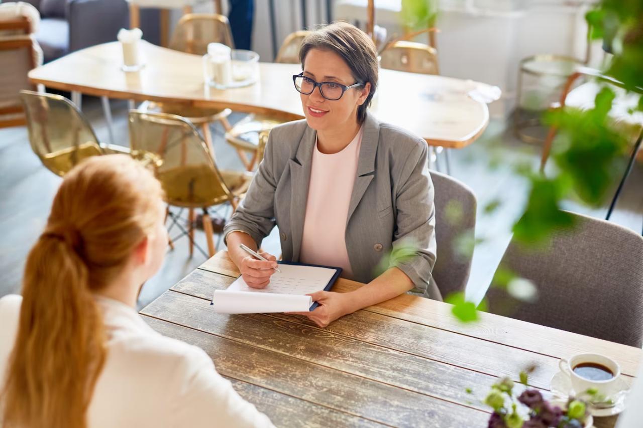 A consultant with a notebook talks with a client across a cafe table.