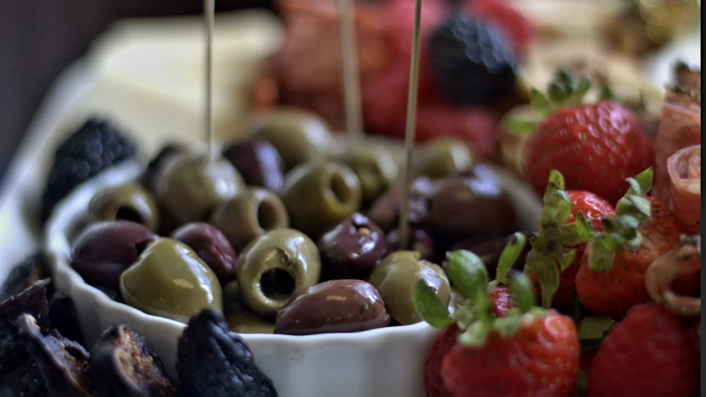 A close-up of mixed olives beside strawberries and sliced meats.